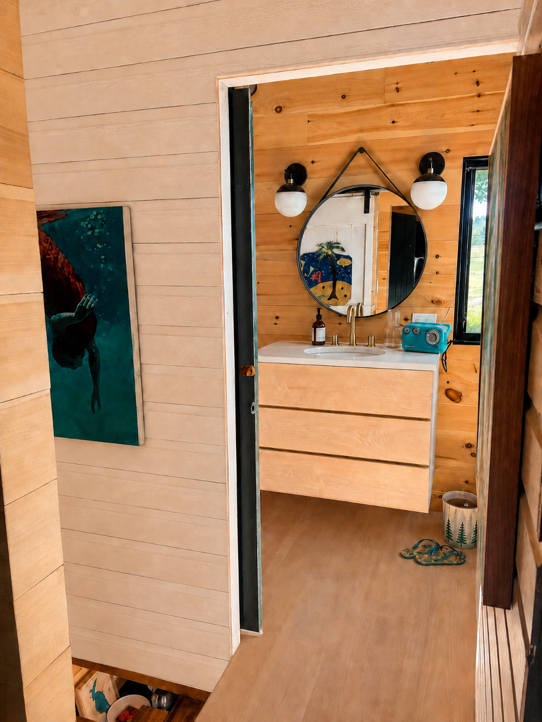 Light wood bathroom vanity with a round mirror and camp-inspired details