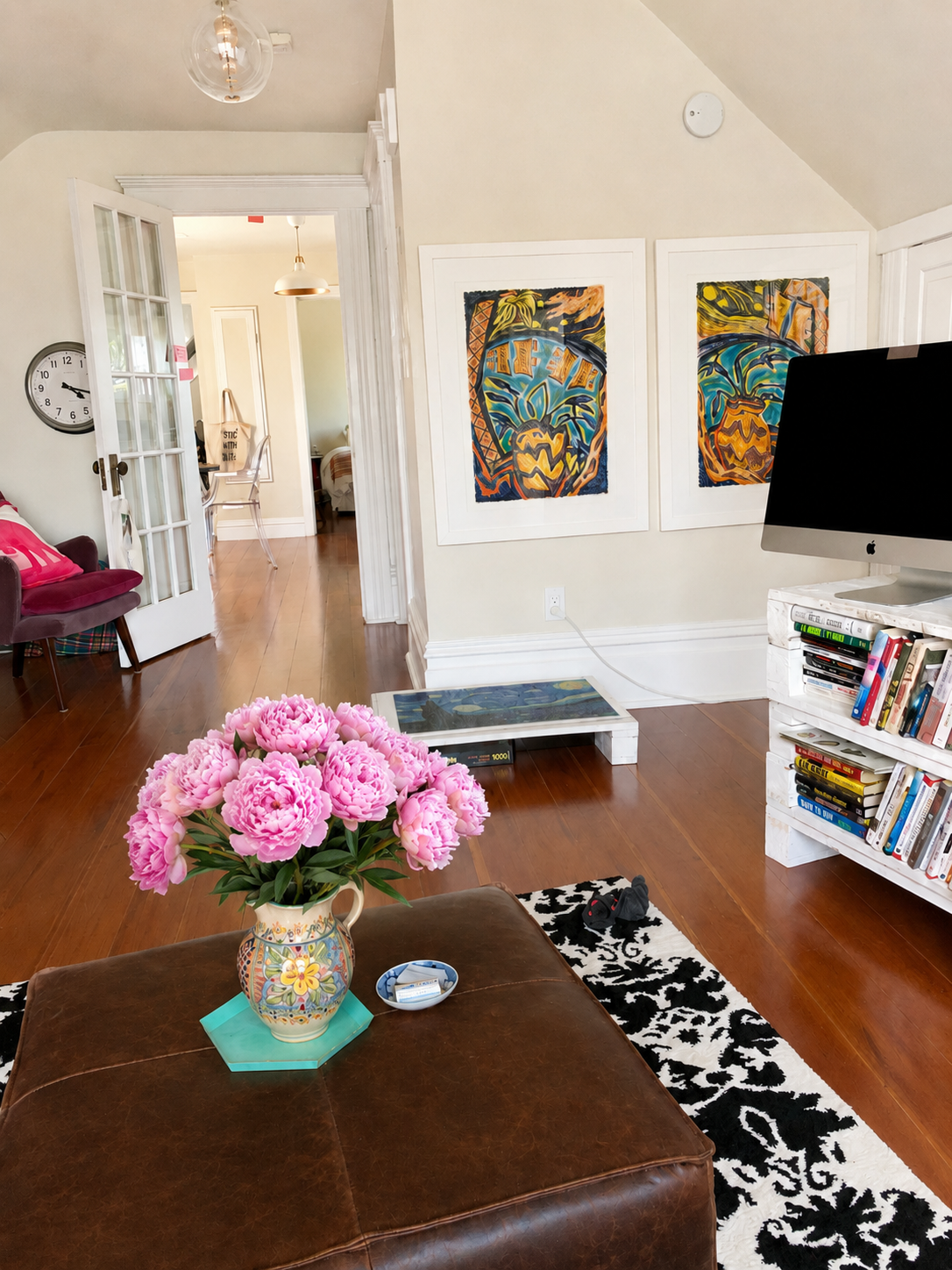 Bright white living room with peonies, hardwood floors, and colorful framed art